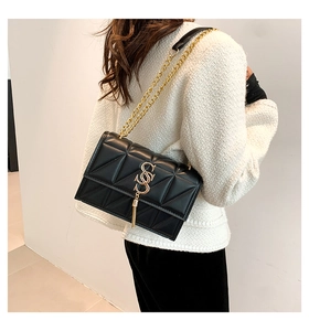 Detail of black quilted shoulder bag featuring gold chain strap and metal tassel accents