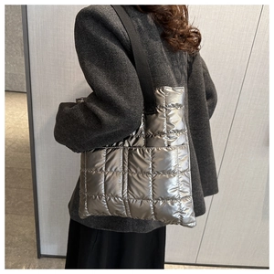 Detail of silver metallic quilted tote bag with wide black strap on grey coat
