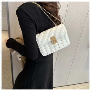 Detail of white quilted crossbody bag with gold chain strap and turn-lock on model
