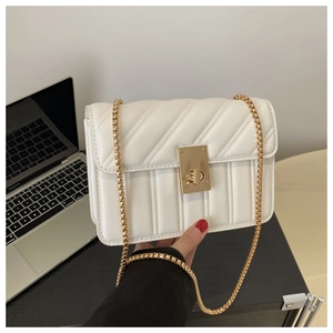Detail of white quilted crossbody bag with golden turn-lock and chain strap on a desk