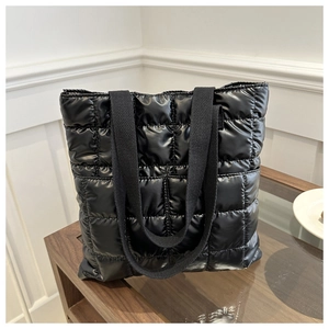 Detail of black quilted puffer tote bag with glossy nylon finish and wide webbed straps