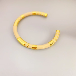 Minimalist bamboo-shaped gold-plated bangle with cream enamel accents on grey background
