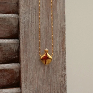 Elegant gold pomegranate necklace with pearl accent and hammered texture on wooden backdrop
