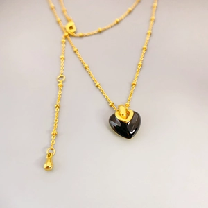 Detail of gold heart pendant necklace with black enamel center and bead chain
