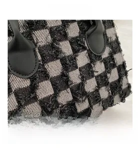 Close-up of black and grey plaid tweed bag with frayed fringe edges and leather detail