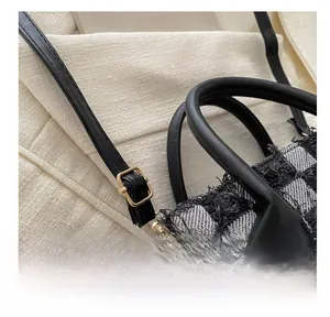 Detail of checkered denim bag showing fringe edges and adjustable gold metal buckle