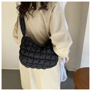 Close-up of black quilted puffy cloud bag worn with a classic beige trench coat