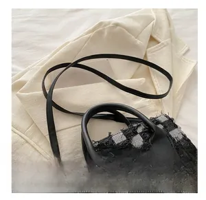 Close-up of black and white checkered tweed handbag with leather handles and slim strap