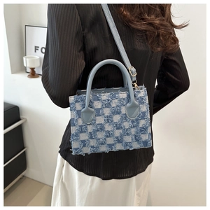 Detail of blue checkerboard denim handbag featuring fringed edges and textured tassels