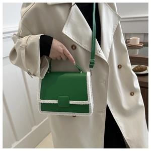 Dark green leather crossbody bag with white faux shearling trim on a beige trench coat