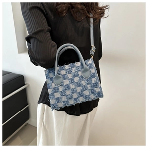 Detail of checkered denim crossbody bag with fringe edges and light blue strap