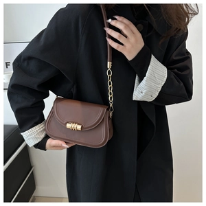 Detail of vintage brown leather handbag with gold clasp and chain strap on black coat