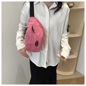 Pink nylon fanny pack with dual zippers and adjustable black strap worn over a white shirt