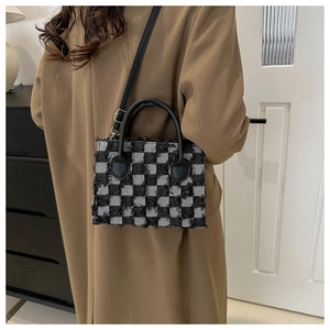Detail of checkered denim handbag with fringe edges and leather strap on trench coat