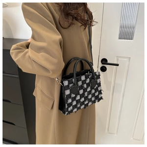 Detail of checkered tote bag with fringe edges styled with a brown coat for fall fashion