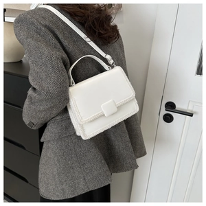 Detailed view of white structured handbag with faux fur trim and adjustable strap