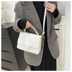 Close-up of a white patent leather handbag with plush faux fur trim and square buckle