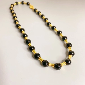 Collier à maillons en bambou doré avec onyx noir et perles sur un fond gris clair