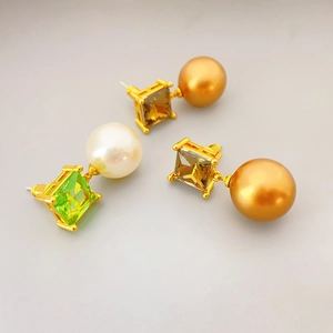 Detailed close-up of square cut crystals and round pearl pendants on gold-plated earrings