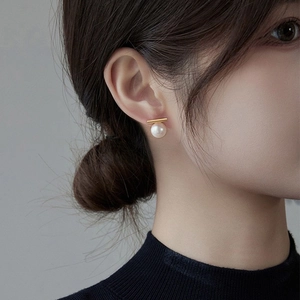 Detailed close-up of a minimalist pearl stud earring with a gold horizontal bar on ear