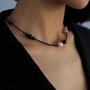 Collier en perles baroques et oeil de tigre porté sur un blazer noir élégant