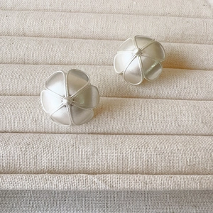 Elegant silver matte flower earrings with freshwater pearl centers on a textured beige tray