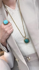 Close-up of vintage square turquoise pendant and ring with braided gold edges on a model
