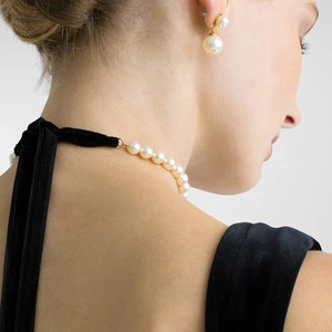 Detail of elegant pearl necklace with black velvet ribbon and matching earrings on a model