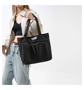 Detail of a black nylon tote bag with front pockets and a detachable coin purse hanging