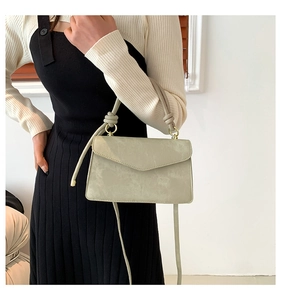 Detail of knotted handle and envelope flap on a sage green suede texture handbag