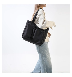 Detail of black nylon tote bag featuring multiple front utility pockets and fashion label