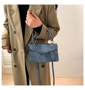 Close-up of a blue vintage textured crossbody bag with knotted handle on a beige trench coat