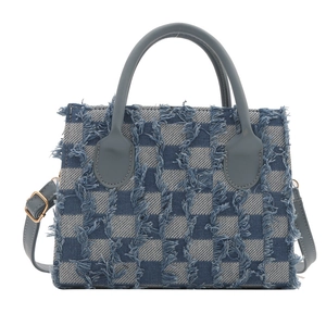 Blue checkerboard denim handbag with fringe details and leather handles on white background