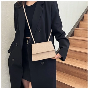 Borsa a tracolla beige coccodrillo indossata su blazer nero per un look minimalista