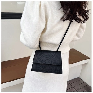 Piccola borsa a tracolla nera in feltro con motivo a coccodrillo su vestito bianco