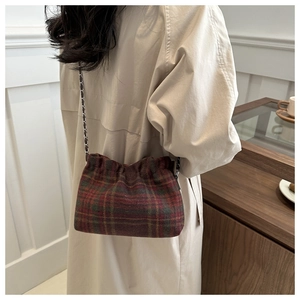 Close-up of vintage red and green plaid crossbody bag with a gold chain strap on model