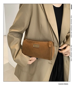Détail du sac polochon en daim marron montrant la texture mate et la bandoulière fine