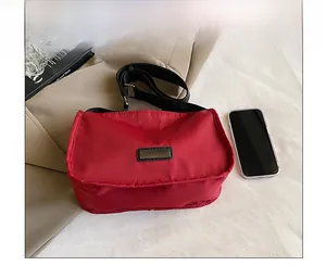 Red nylon crossbody bag with wide black strap shown next to a phone for size comparison