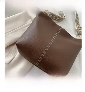Close-up of brown bucket bag with white contrast stitching and patterned wide strap