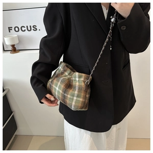 Model wearing a green plaid wool bucket bag with silver chain strap and pleated texture
