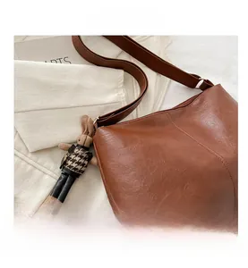 Detailaufnahme der braunen Handtasche mit Kieselleder und kariertem Hasenanhänger