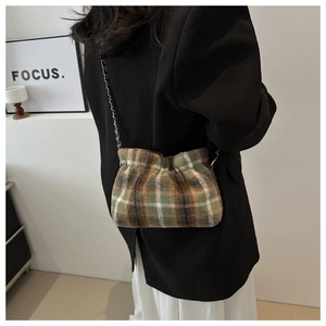 Detail of checkered tweed bucket bag with silver chain worn over a black blazer