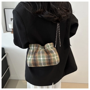 Detail of plaid wool bucket bag with metal chain strap worn over a black blazer