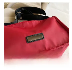 Detail shot of the rectangular metal logo plate on red nylon crossbody bag with black strap