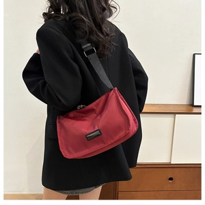 Detail of red nylon crossbody bag with black adjustable strap worn by a model