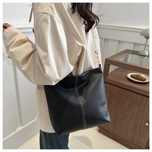 Detail of black pebbled leather bucket bag with white contrast stitching and gold buckle