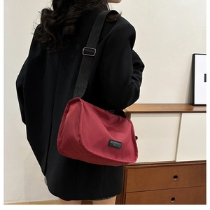 Red nylon crossbody bag with wide black strap and logo patch shown on a black blazer