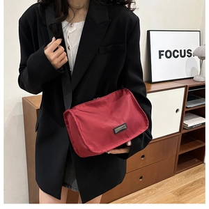 Detailed shot of red nylon crossbody bag with black wide strap and metal logo plaque