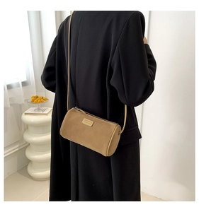 Sac bandoulière cylindrique en suédine marron présenté dans un décor chic