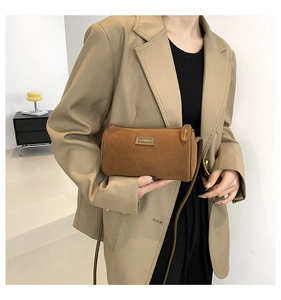 Borsa a tracolla cilindrica in camoscio marrone indossata da una modella per un look moderno